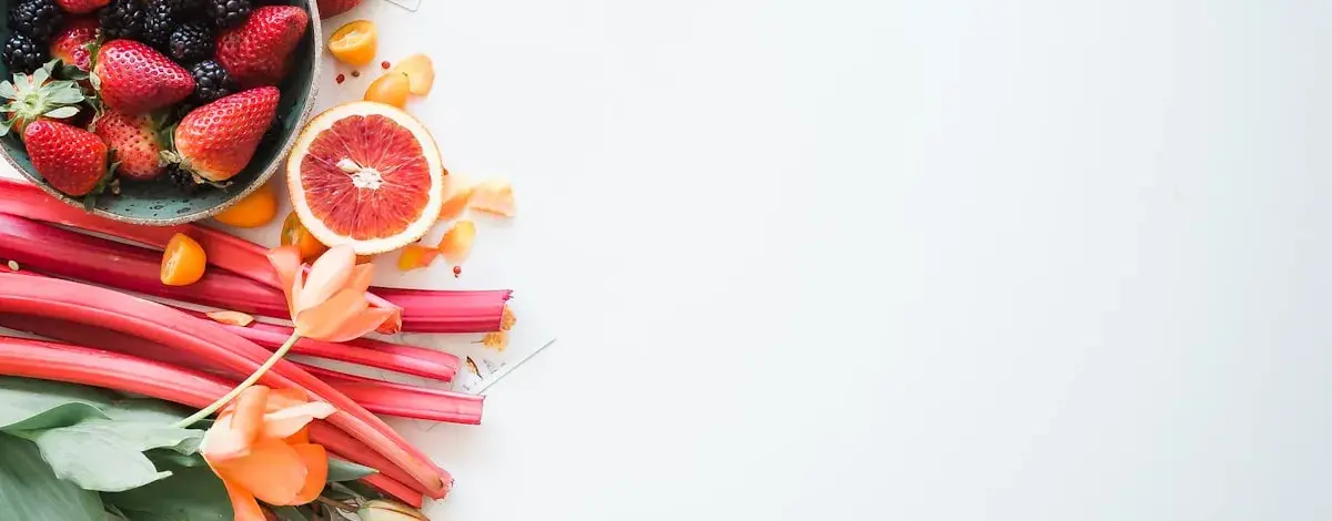 Fraises, m&ucirc;res, rhubarbe et orange sanguine dispos&eacute;es &agrave; gauche d'une table claire.