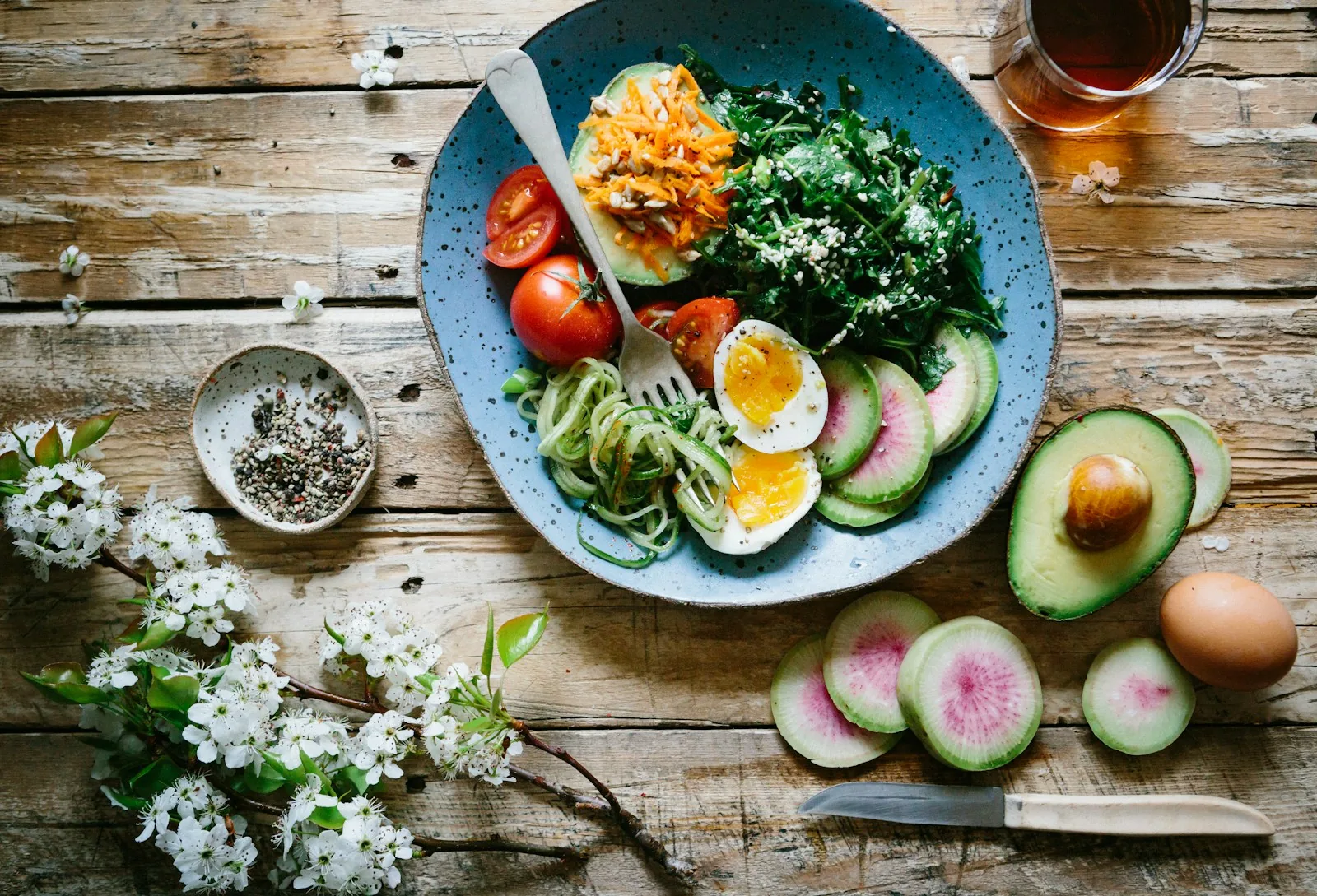 Bol d'ingr&eacute;dients frais, l&eacute;gumes, &oelig;uf, avocat, fleurs blanches sur table en bois